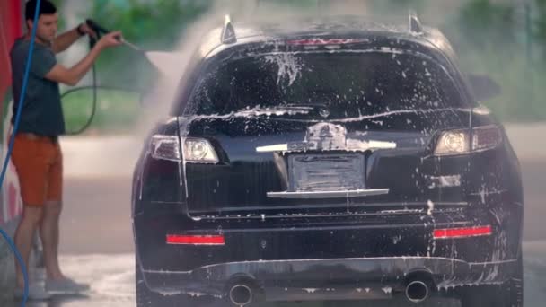 Μαύρο αυτοκίνητο πλένεται από έναν νεαρό άντρα — Αρχείο Βίντεο