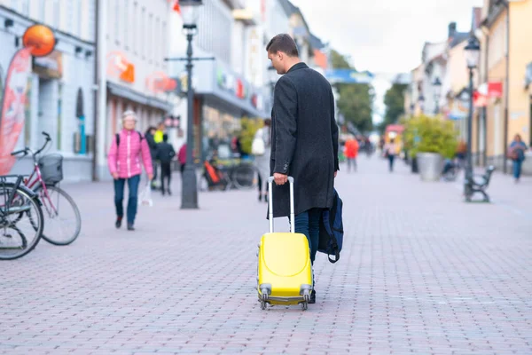 Young man wheeling a suitcase down a street — Stock Photo, Image