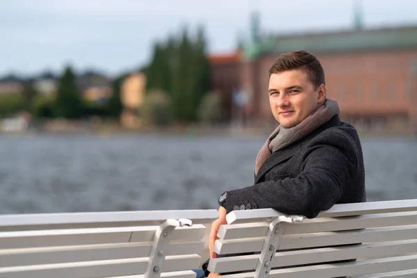 Aantrekkelijke jongeman zittend op een bankje buiten — Stockfoto