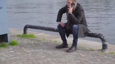 Genç adam cep telefonu kullanarak bir kordonun üzerinde oturuyor.