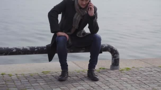 Young man in overcoat using a mobile outdoors — Stock Video