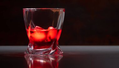 Kaliteli bir bardakta buzlu, sade bir brendi, yansıtıcı bir tezgahta, düşük açılı, arka planda fotokopi alanı olan bir bardakta.