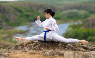 Kickboks eğitimi alan genç bir kadın vadiye ve nehre bakan bir kayada hareket kabiliyetini ve esnekliğini arttırmak için ikiye ayrılıyor.