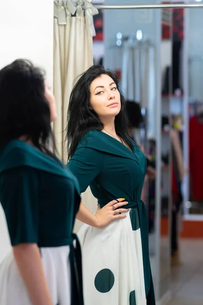 ブティックストアで服を試着魅力的な女性は彼女の反射に焦点を当て フィッティングルームで鏡の中に新しいドレスを評価 — ストック写真