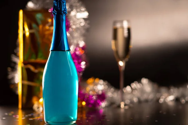 スパークリングワインとカラフルなきらびやかな装飾のフルートの前でシャンパンのカラフルな青いボトルとパーティー 新年やクリスマスのコンセプト — ストック写真