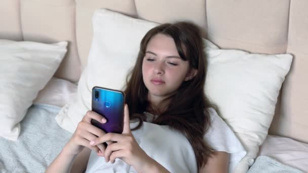 Žena relaxuje na posteli se svým smartphonem — Stock video