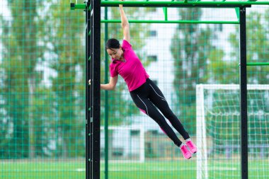 İnce tonlu, açık hava spor aletleri üzerinde çalışan genç bir kadın paralel barlar ve merdiveni kullanarak sağlık ve zindelik ya da telif alanı ile aktif yaşam tarzı kavramı kullanarak spor yapıyor.