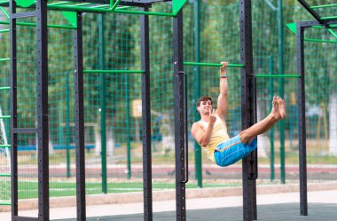 Genç erkek sporcu, şehirdeki açık hava spor tesisinde sağlık ve spor salonunda ya da aktif yaşam tarzı kavramında paralel barlarda çalışırken yumruğuyla hareket ediyor.