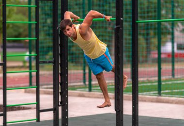 Açık hava spor salonunda çalışan sağlıklı bir genç, paralel barı kullanarak kol ve vücut kaslarını sağlıklı ve sağlıklı bir konseptte güçlendirir.