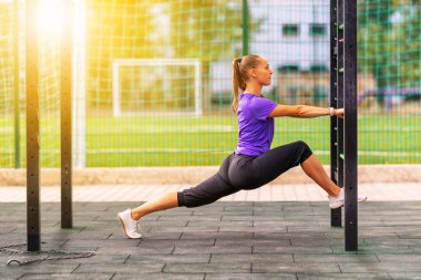 Genç bir kadın şehir parkında spor merdiveni kullanarak poz veriyor. Sıcak bir güneş, sağlık ve zindelik ya da aktif bir yaşam tarzı kavramının arkasına ışık tutuyor.