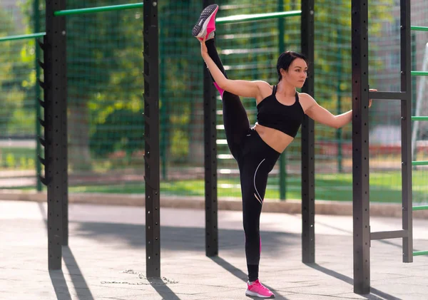 Supple young woman doing the vertical splits outdoors in an open air gym at a sporting facility in a health and fitness concept