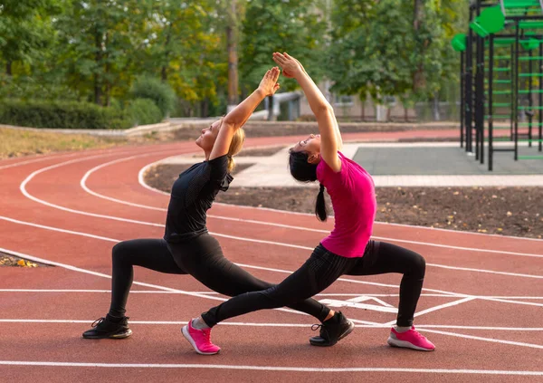 Two Young Woman Doing Synchronised Yoga Forward Lunge Poses Outdoors — Stock Photo, Image