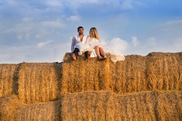 在天空的背景上, 新郎新娘坐在一个大干草堆上 图库照片
