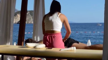 Tanınmayan kadın masöz hafifçe spa tedavisi seçim çerçevesi veya gölgelik sahilde, ağır çekim gölgesinde yatan adam geri Masaj