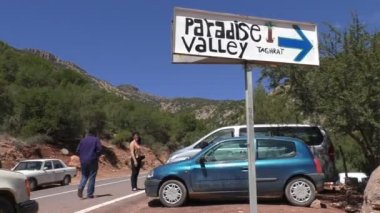Fas, Afrika yolda yön işareti Paradise Valley için; Adam yavaş yavaş üzerinde park edilmiş yol kenarında arabada bekleyen kadın doğru yürüyor