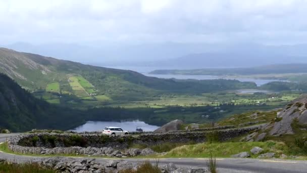 アイルランドのHealy Passからの高い角度の景色 白い車はグランモア湖とケンマーレ湾の上の道路R574上の背景に運転しています — ストック動画
