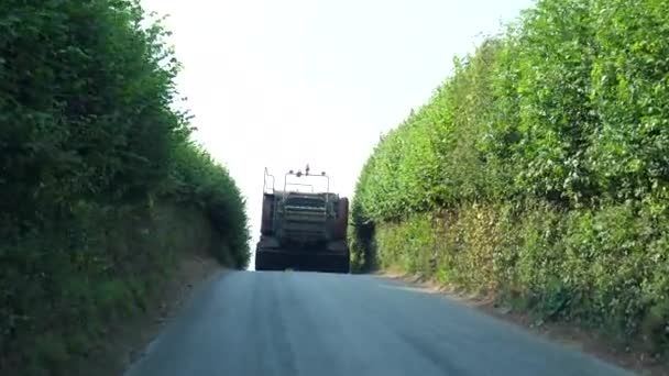 イングランド南部の狭い田舎道や車線で大規模なローカルファームトラクターの後ろに運転車のフロントガラスビュー — ストック動画