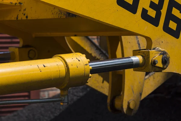 Shiny hydraulic cylinder rod of yellow road machinery close-up