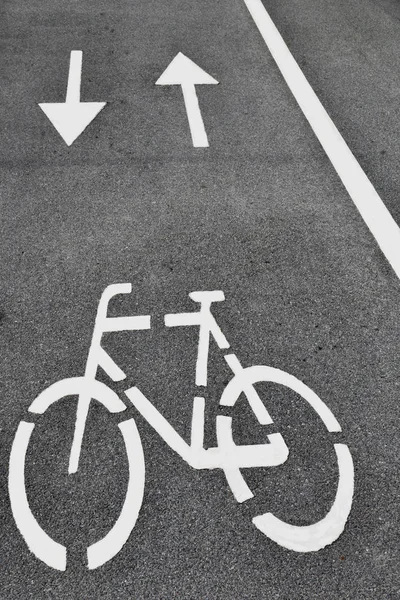White arrows and bicycle sign on grey lanes road.