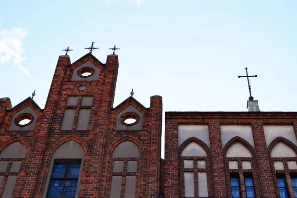 Fragment of old  historical red brick church building facade with decorative details and cross on light sky background close up view.