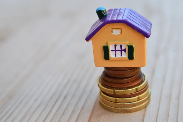 Property investment, house mortgage and money saving financial concept with copy space for text. Colorful house on money coin stack on natural blurred wood background.