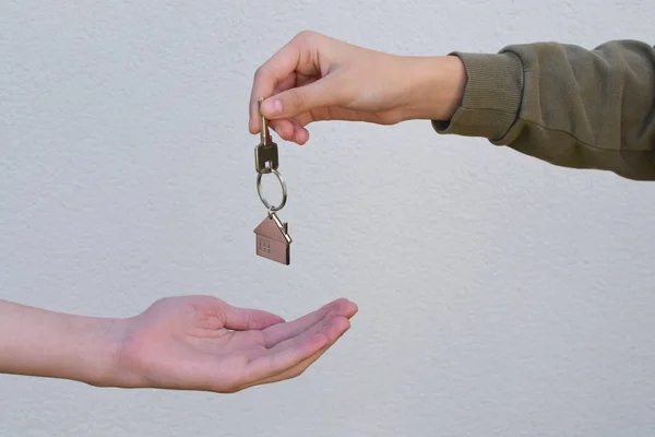 Hand giving to another person home or apartment keys with house shaped keychain on white background with copy space for text. Real estate, buying and moving new home or renting property concept.