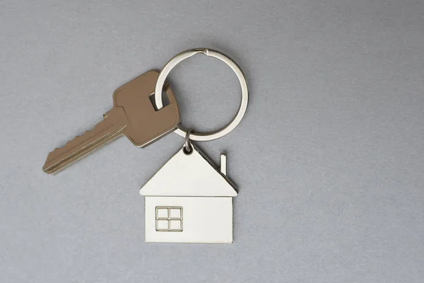 Key with metal house shaped pendant on grey background closeup view with copy space for text. Real estate, buying and moving new home or renting property concept.