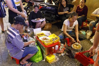 Vietnamlılar sokakta oturup Saygon, Viet'te yemek hazırlıyorlar.