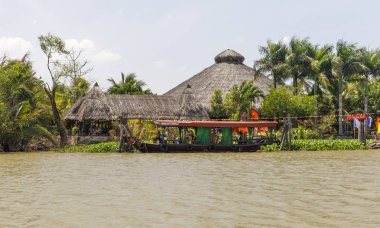 Tekne ve Mekong nehir kenarında büyük bir saz çatılı bina 