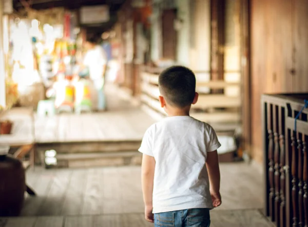 Kid boy wearing sweatshirt over isolated background walking backwards looking away . He is trying to look for the place and he could\'t find it concept.Blurred market outdoor background