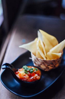 Ahşap masada domates salsa ve mısır cipsi , Serrano biber, kırmızı soğan, yeşil soğan, kireç ve siyah çanak kişniş ile taze domates salsa