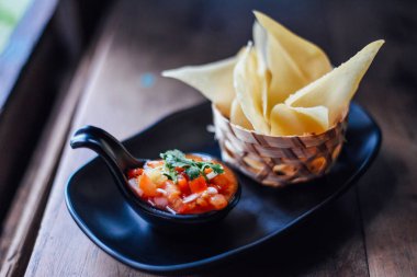 Ahşap masada domates salsa ve mısır cipsi , Serrano biber, kırmızı soğan, yeşil soğan, kireç ve siyah çanak kişniş ile taze domates salsa