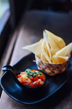 Ahşap masada domates salsa ve mısır cipsi , Serrano biber, kırmızı soğan, yeşil soğan, kireç ve siyah çanak kişniş ile taze domates salsa