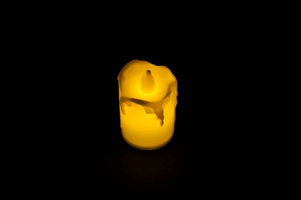 White candle on black background isolated. Small candle with light yellow spots on light background. Christmas decor