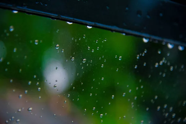 Drops of rain on glass with green tree nature background,romantic shot scene content,colorful raindrops.Blurred leaves of trees