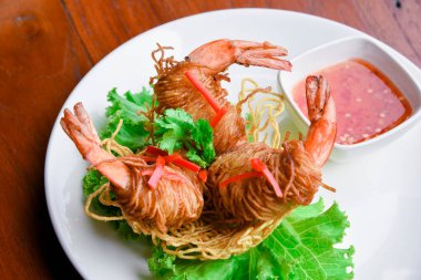 Goong Sarong eriştesi ambalajlı karides gevrek erişte, sebze ve sos ahşap masada beyaz tabak, Tayland yemeği.