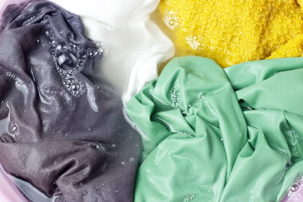 Vêtements colorés lavés avec un lavabo avec bulles de savon, gros plan, vue sur le dessus — Photo