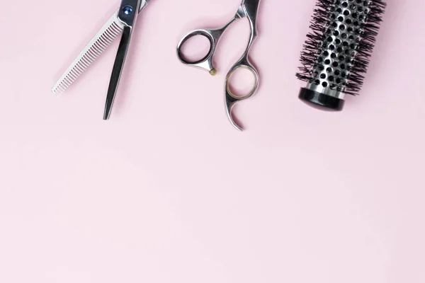 Scissors and comb on a pink background, copy space
