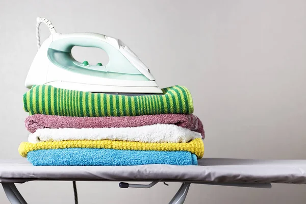 Järn och en bunt med handdukar på strykbräda, grå bakgrund — Stockfoto