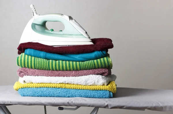 Iron and a stack of towels on the ironing board, gray background — Stock Photo, Image