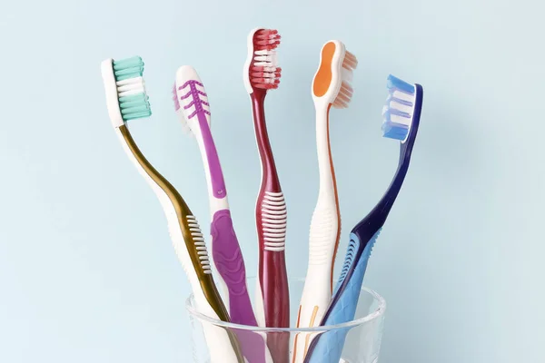 Escovas de dentes multicoloridas em um copo de vidro vista frontal, fundo azul — Fotografia de Stock
