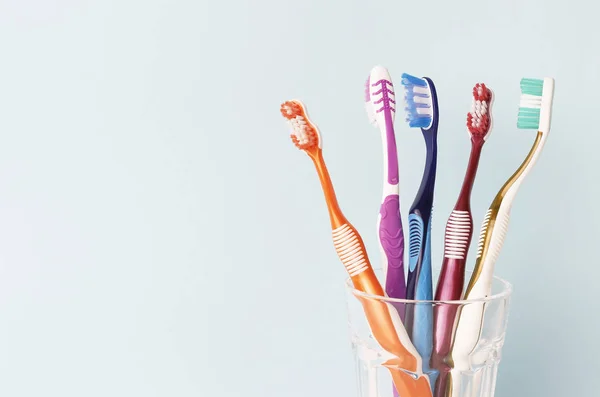 Escovas de dentes multicoloridas em um copo de vidro, fundo azul — Fotografia de Stock