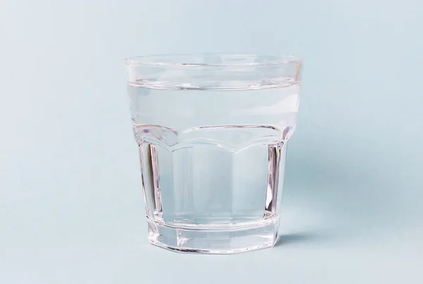 Cangkir kaca dengan air pada latar belakang biru — Stok Foto
