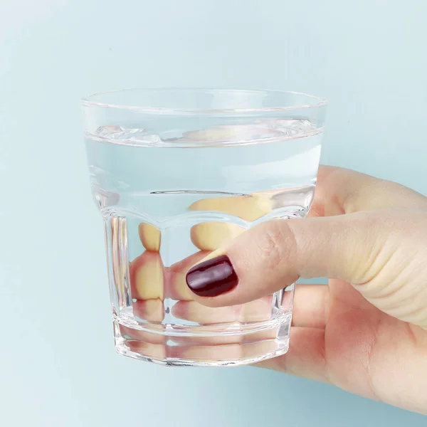 Tangan wanita memegang gelas dengan air, latar belakang biru — Stok Foto