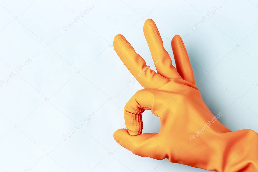 Female hand in orange rubber gloves shows ok sign, blue background