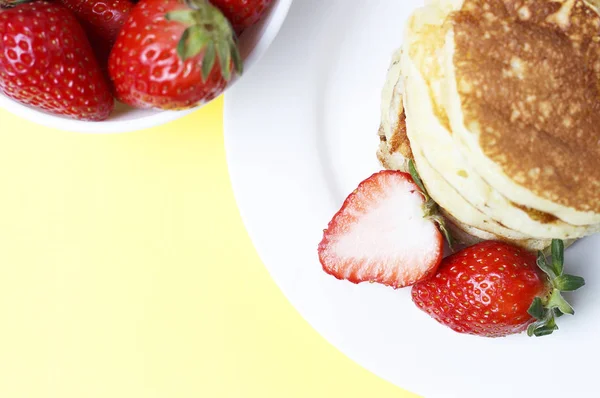 Pancakes on a plate and strawberries on a yellow background, top view — Stock Photo, Image