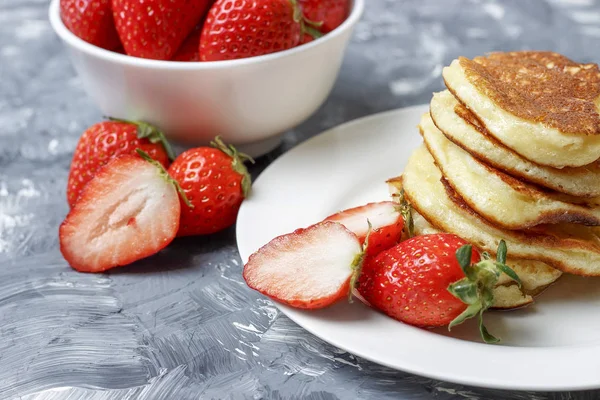 Pfannkuchen auf einem Teller und Erdbeeren auf grauem Hintergrund, Vorderseite — Stockfoto