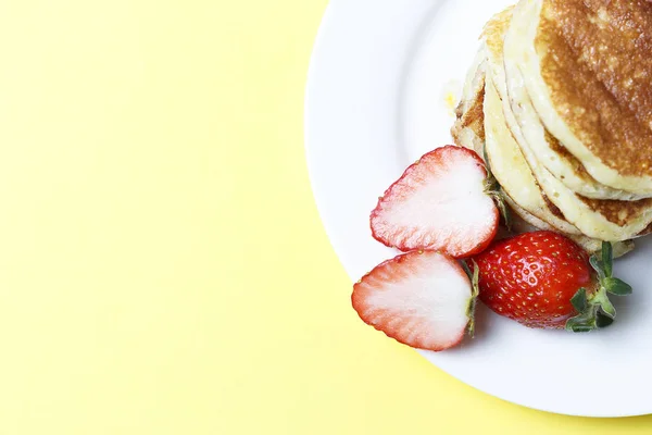 Pfannkuchen auf einem Teller und Erdbeeren auf gelbem Hintergrund, Ansicht von oben — Stockfoto