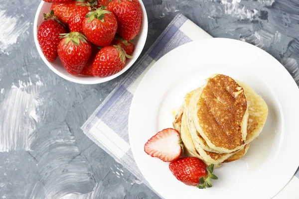Pfannkuchen auf einem Teller und Erdbeeren auf grauem Hintergrund — Stockfoto