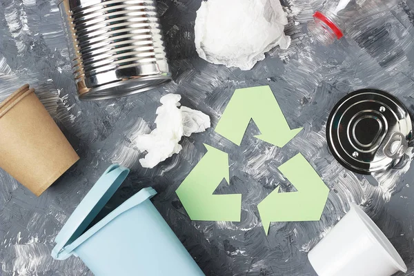Zelený symbol recyklace a plastický odpad, železné smetí na šedém pozadí, pohled shora. — Stock fotografie